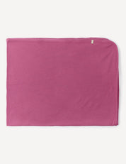 A neatly folded Blanket – Merino Baby AirWool in solid pink, crafted from soft merino wool with a small beige tag in the upper right corner, displayed on a white background.
