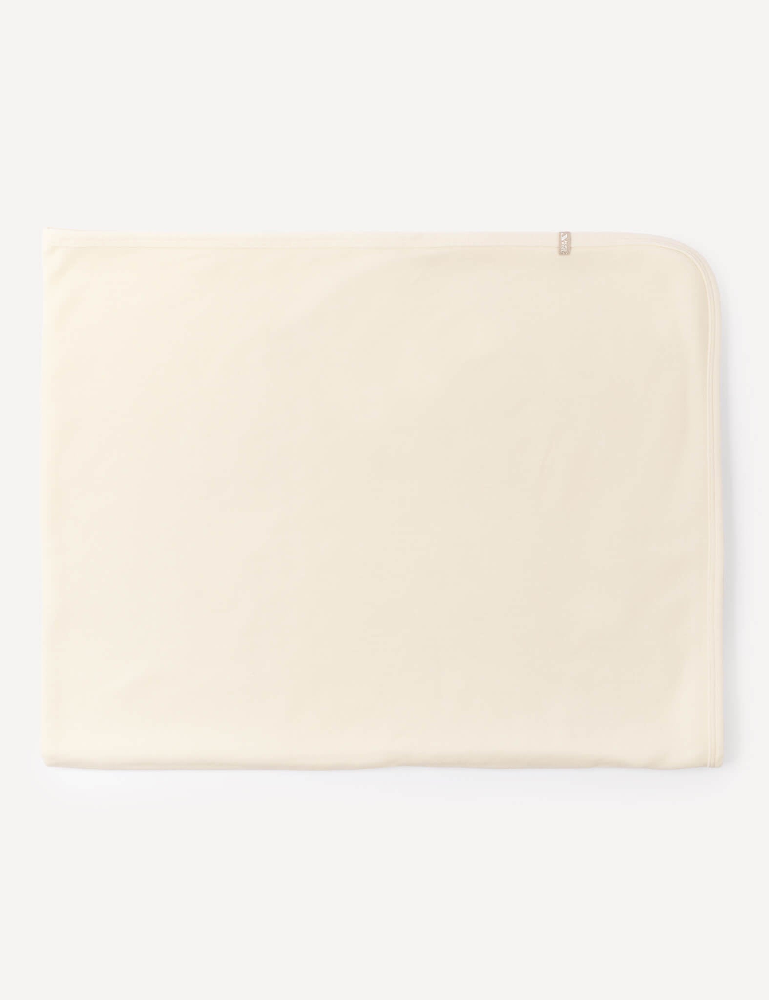 A neatly folded, light beige rectangular Blanket – Merino Baby AirWool made from soft merino wool, featuring a small tag on the top right corner, placed against a plain white background.