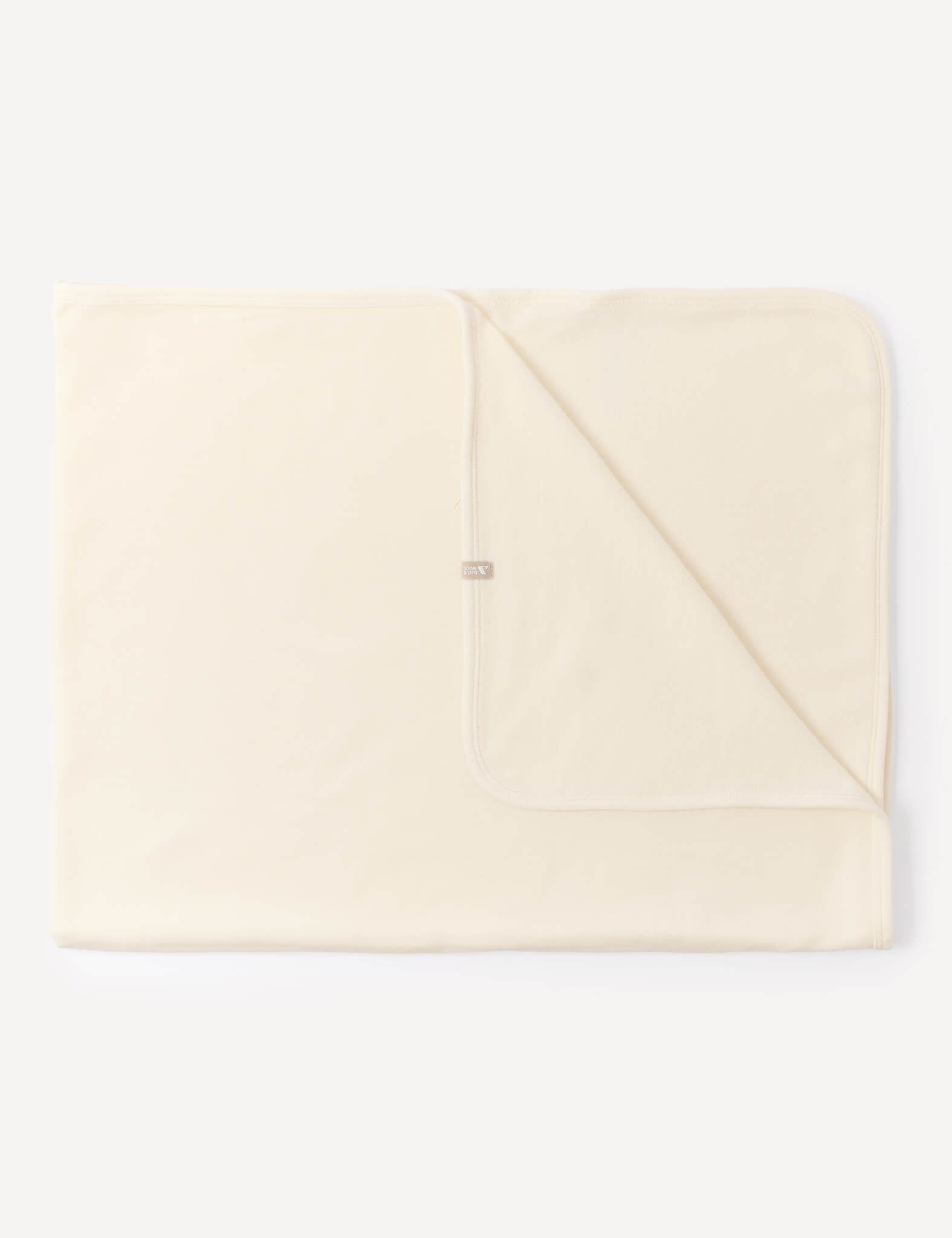 A folded Blanket – Merino Baby AirWool in Marshmallow is laid flat against a white background, with one corner turned over to reveal the underside and a small fabric tag near the edge.