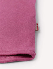 Close-up of the hem of the pink ribbed fabric Jacket – Merino Baby AirWool, possibly a sleeve or pant leg, with a small beige tag featuring red and white stripes visible at the edge. The soft material suggests features like breathable insulation. The background is white.