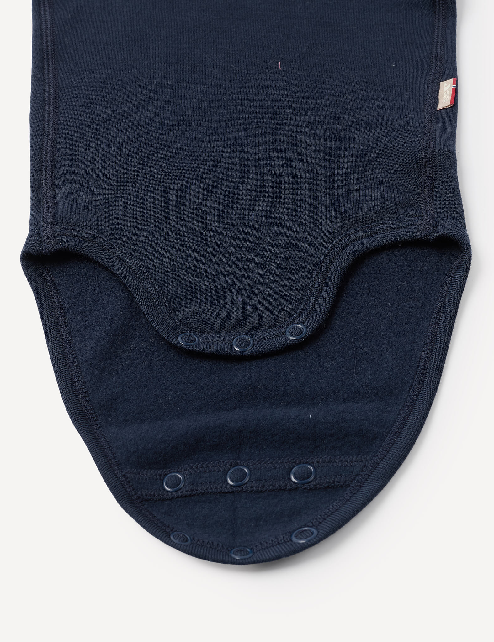 Close-up of the Body – Merino Baby AirWool in navy blue, featuring three snap buttons along its curved bottom edge, displayed against a plain white background.