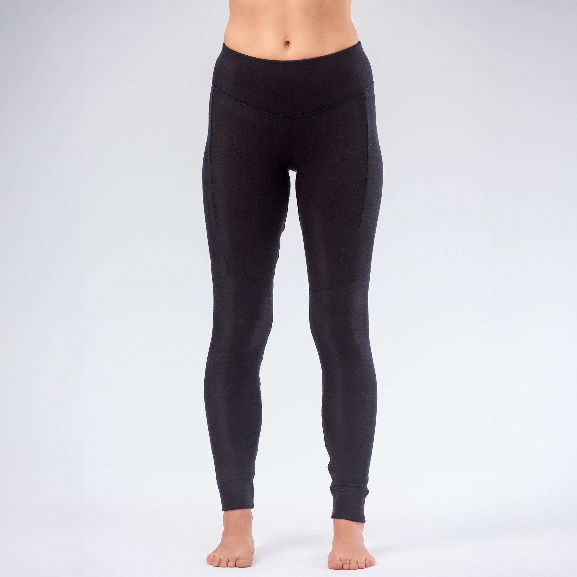 A person stands barefoot against a plain background, wearing high-waisted Leggings Merino – AirWool 260 Women in black. The image is cropped at the upper chest, showing the legs and lower torso.