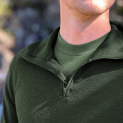 Close-up of a person wearing a Janus Norse Merino Polo in green, with a blurred natural background