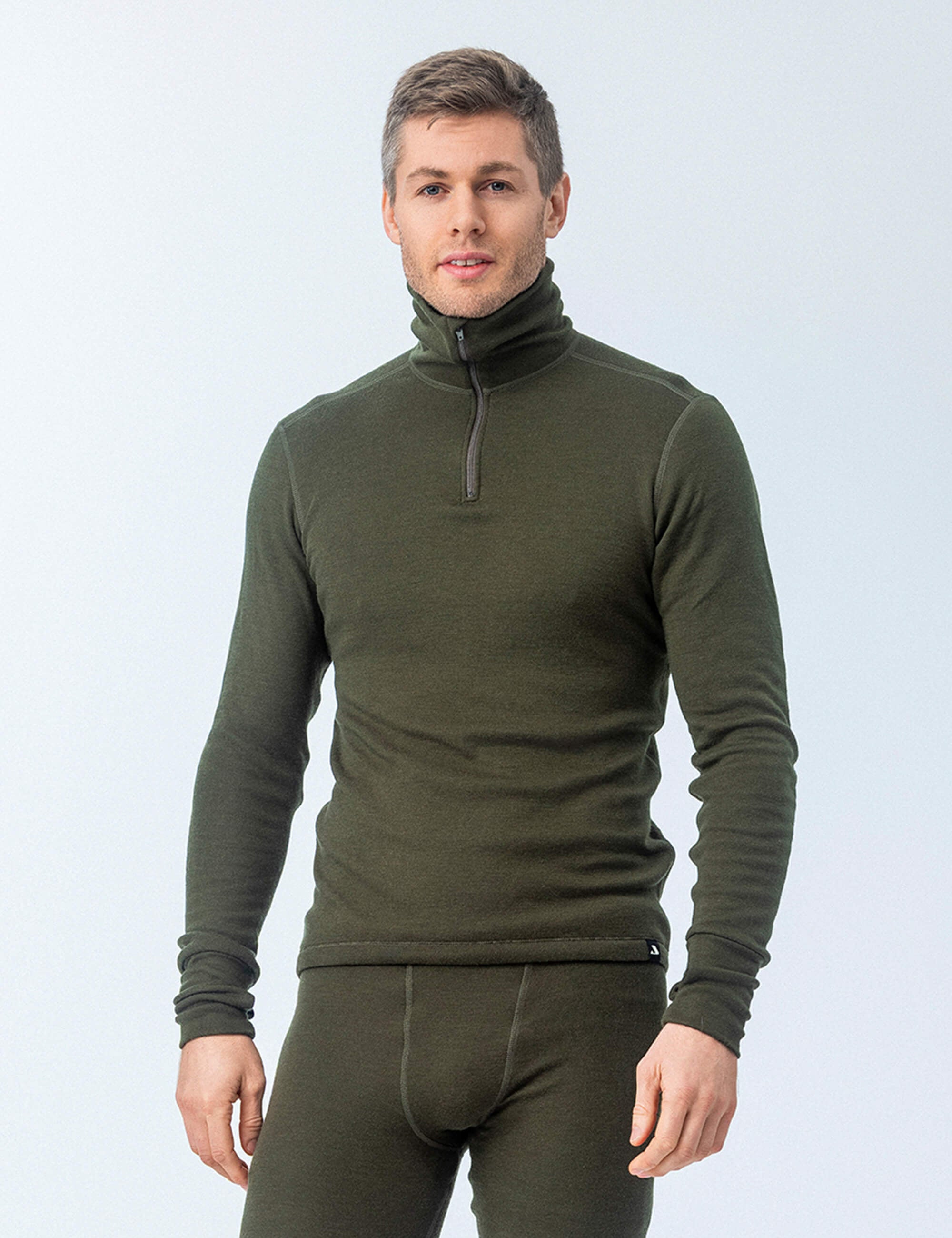 A man wears an olive green Polo with zip wool terry - Norse Merino 210 Unisex quarter-zip top and matching fitted base layer bottoms, ideal for outdoor activities.
