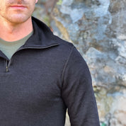 Person wearing a Janus Norse Merino Polo in black, with a blurred natural background