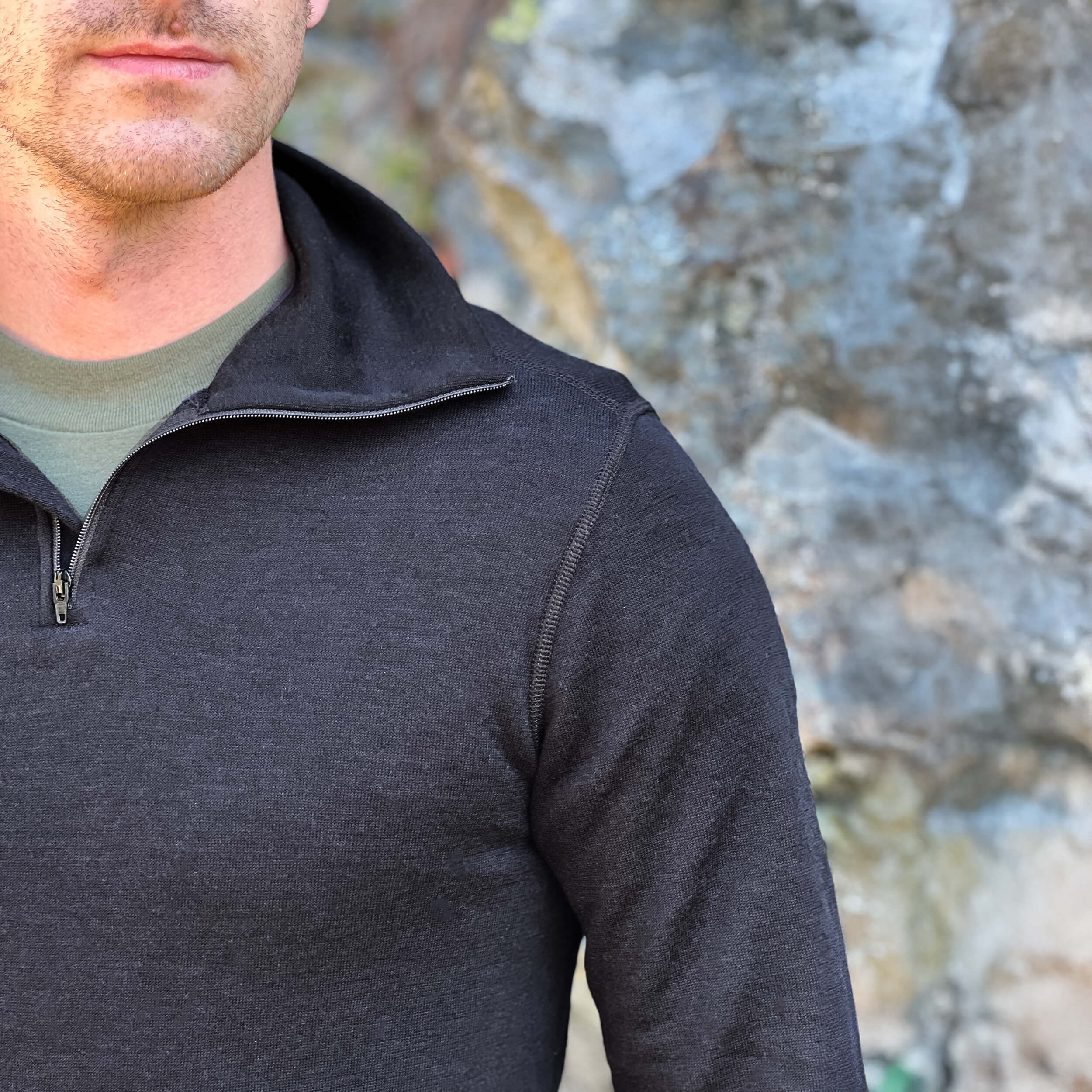 Person wearing a Janus Norse Merino Polo in black, with a blurred natural background