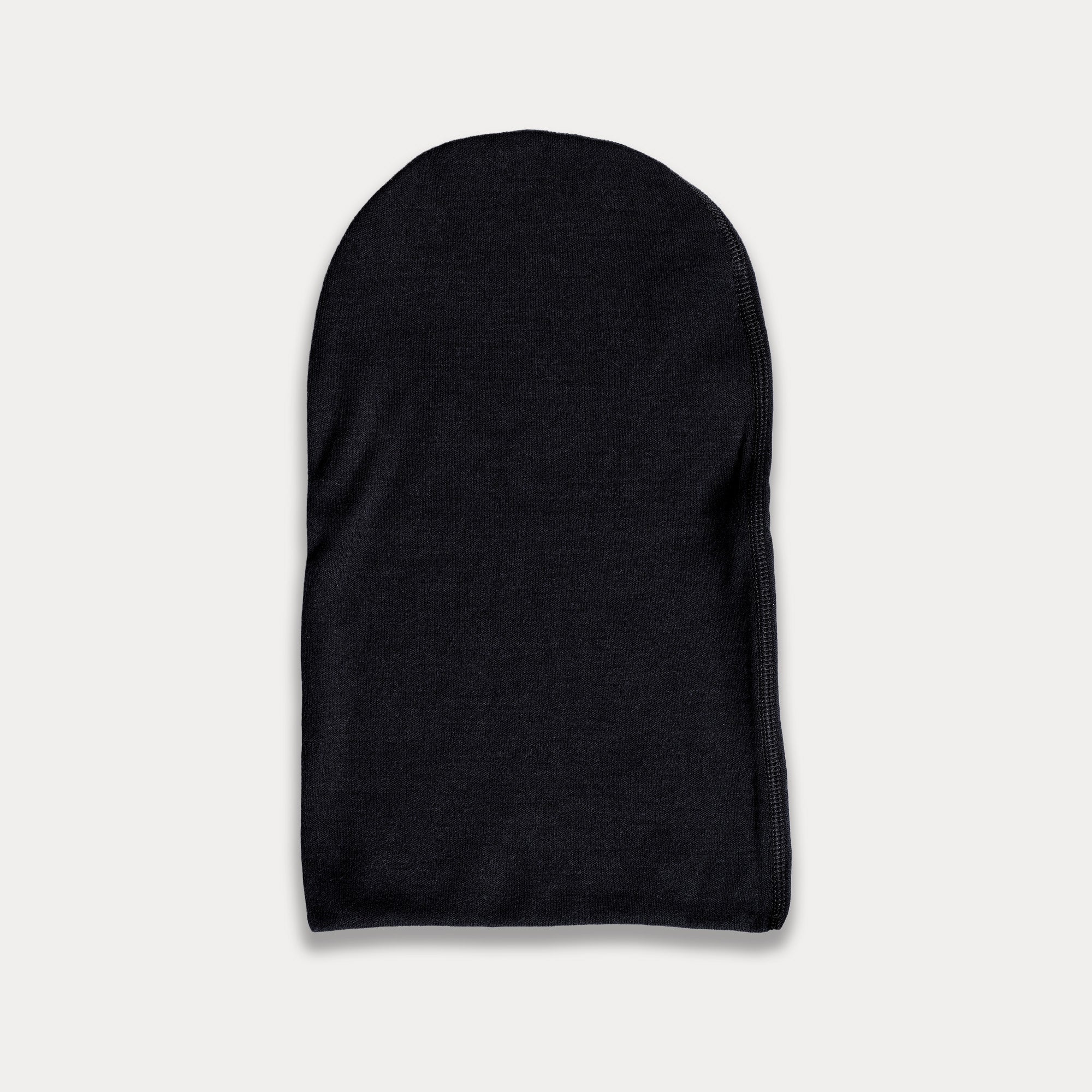 The Watch Cap - Norse Merino 220, shown in plain black merino wool laid flat on a light gray background, features a simple rounded shape with minimal right-edge stitching—ideal for hiking.