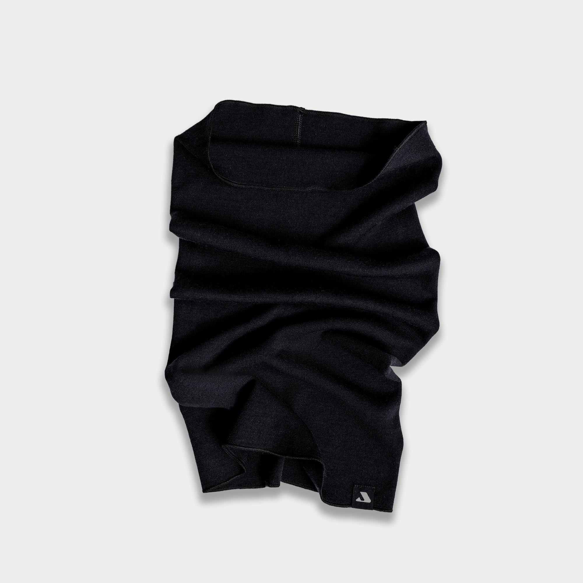 The Headover - Norse Merino 220, a black, odor-resistant neck gaiter made from soft fabric, is laid flat on a light background with slight folds and wrinkles. A small logo tag is visible at the bottom corner.