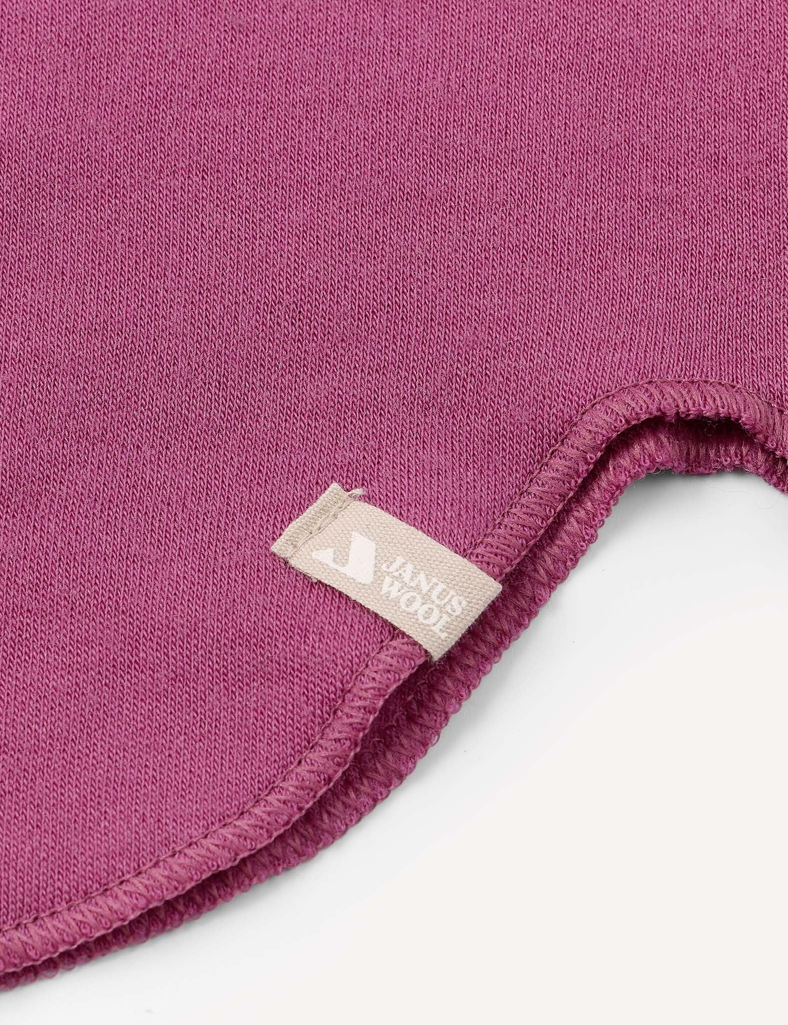 A close-up of a magenta fabric with a curved, stitched edge and a small beige tag attached to the seam, as seen on the Balaclava – Merino Kids AirWool from premium merino wool balaclava collections.