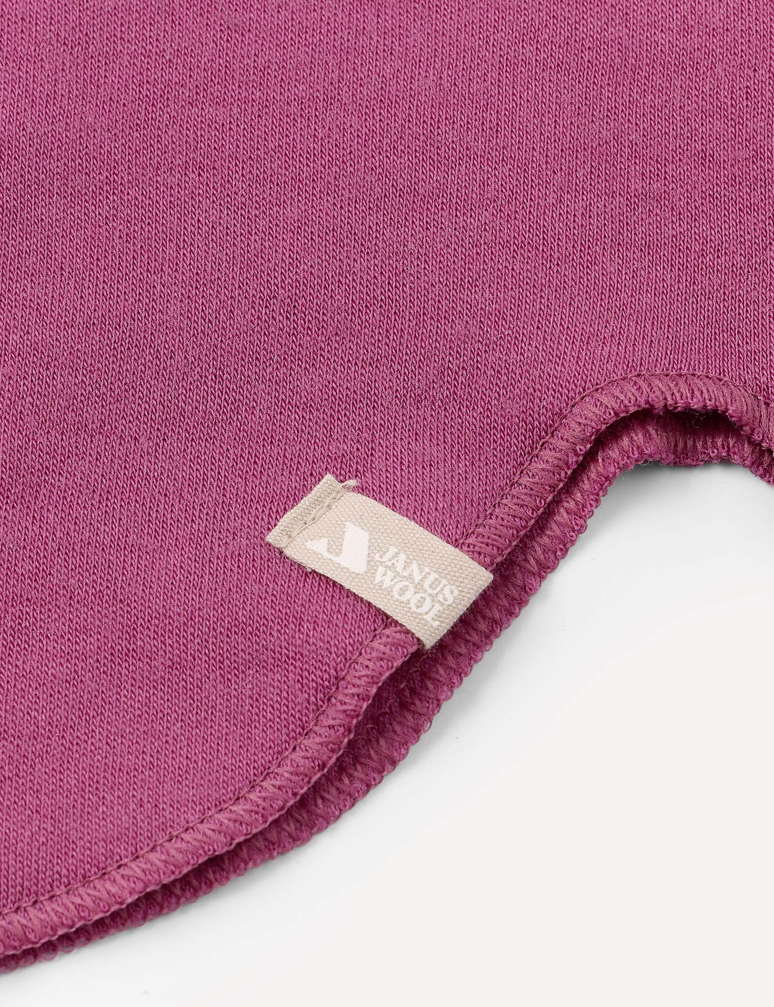 A close-up of a magenta fabric with a curved, stitched edge and a small beige tag attached to the seam, as seen on the Balaclava – Merino Kids AirWool from premium merino wool balaclava collections.