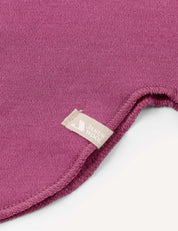 A close-up of a magenta fabric with a curved, stitched edge and a small beige tag attached to the seam, as seen on the Balaclava – Merino Kids AirWool from premium merino wool balaclava collections.
