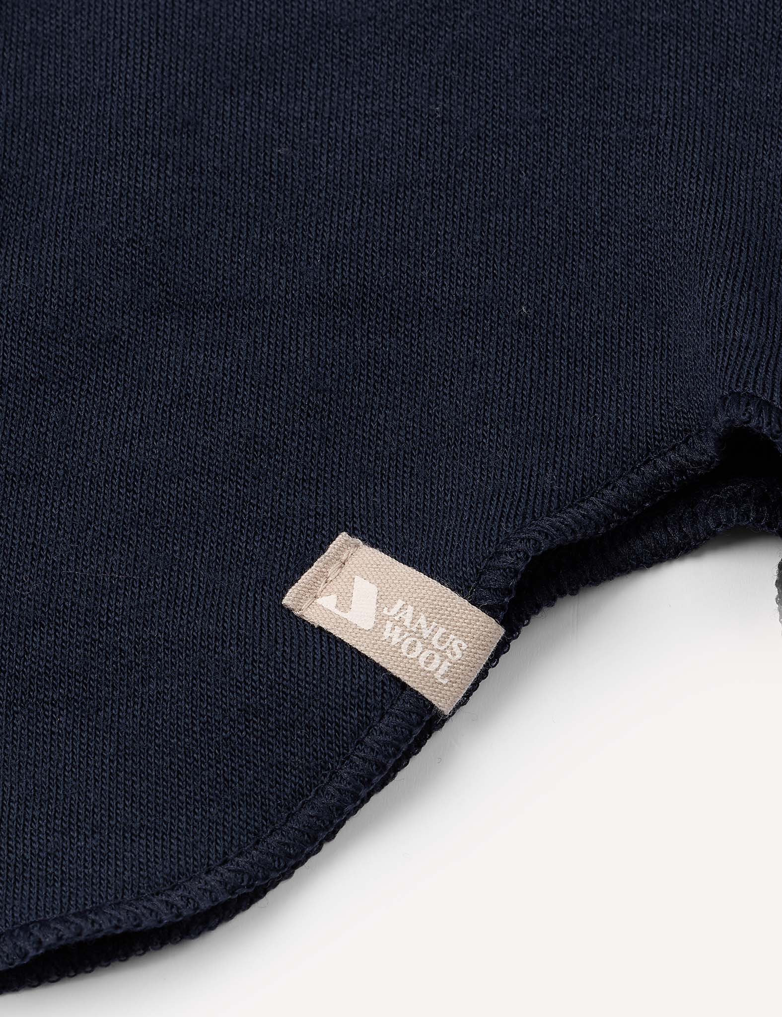 Close-up of a dark blue knitted fabric with a beige label sewn onto the edge, set against a white background. The texture highlights the premium quality of the Merino Kids AirWool balaclava, designed to keep children warm on chilly days.