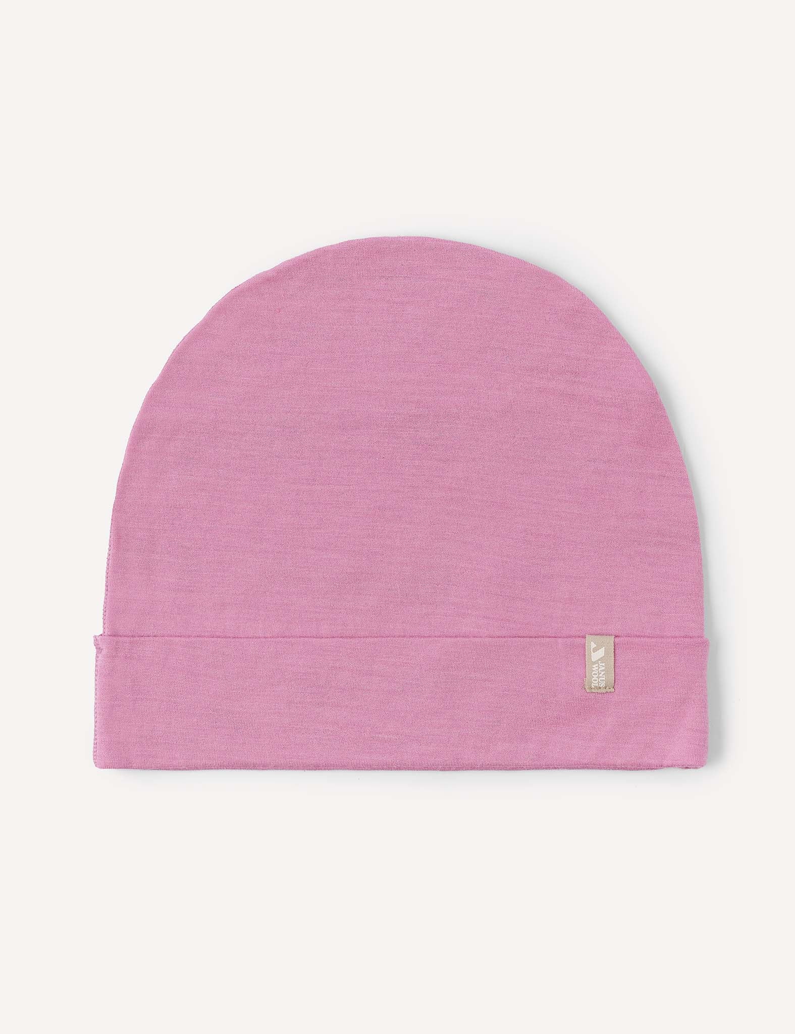 A Beanie – Merino Kids Light in the color Mauve Orchid is laid flat on a white background, featuring a small beige tag with subtle writing attached to its folded edge.