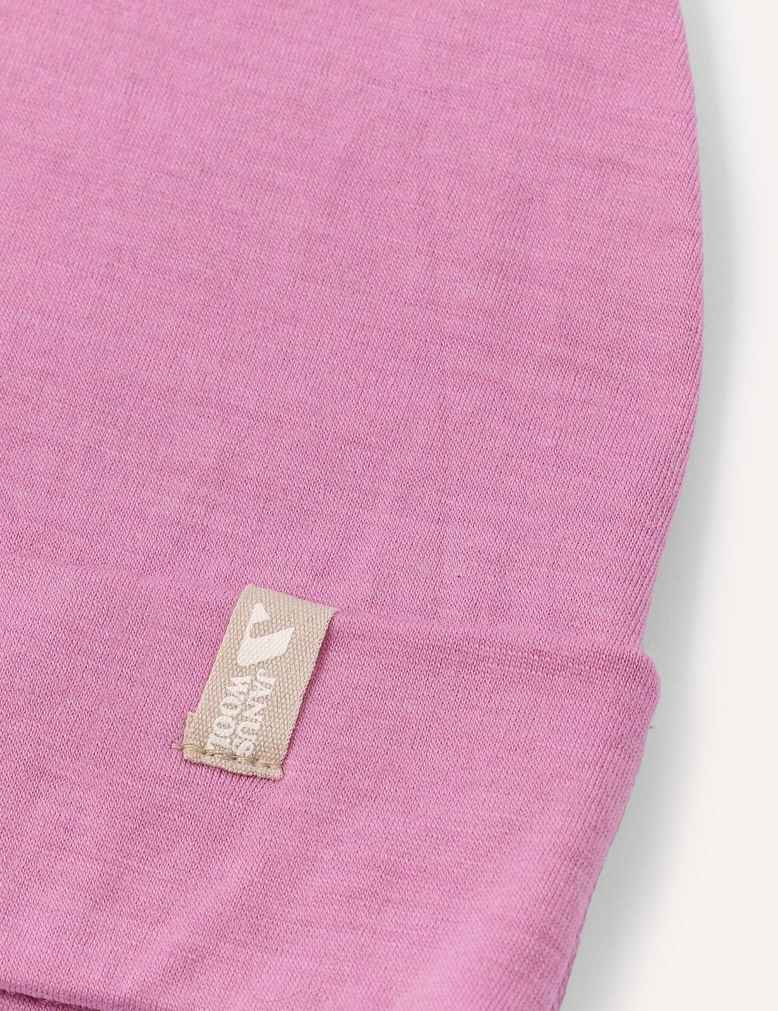 Close-up of the Beanie – Merino Kids Light in pink, featuring a beige tag sewn onto the edge with a logo and text.