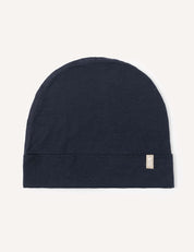 The Beanie – Merino Kids Light in navy is laid flat on a light background, with a small beige tag attached to the folded edge on the right side.