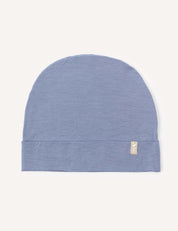 A soft merino wool beanie in the color Troposphere, featuring a small beige tag on the cuff, is displayed flat on a plain white background.
