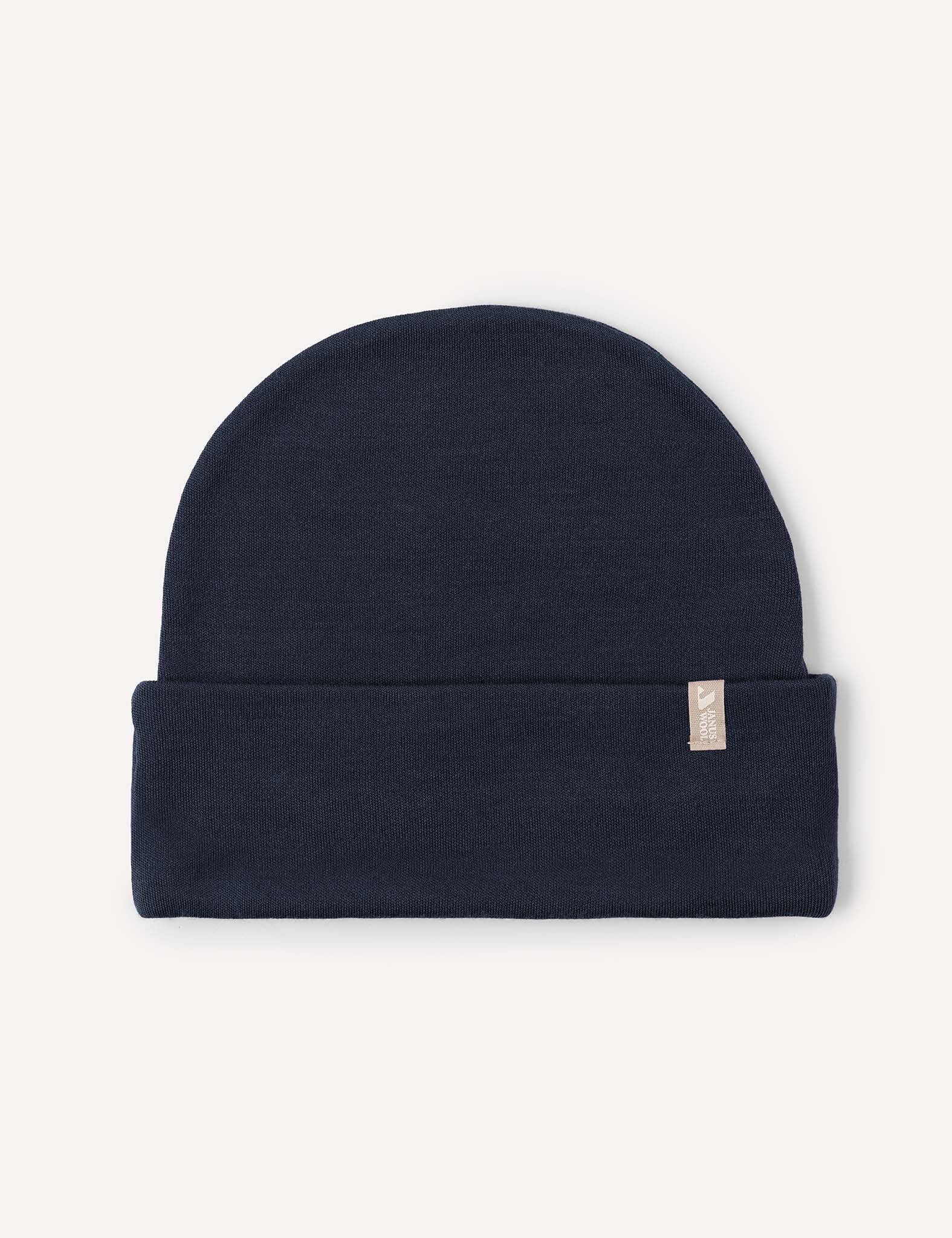 The Beanie – Merino Kids AirWool in Navy is folded flat with a small beige tag on the cuff, displayed on a light background. Made from breathable merino wool, this beanie provides extra warmth for chilly days.