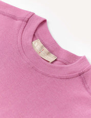 A close-up of the Crewneck – Merino Kids Classic Rib in pink, crafted from ribbed wool jersey, featuring visible stitching and a beige fabric tag at the neckline, displayed against a white background.