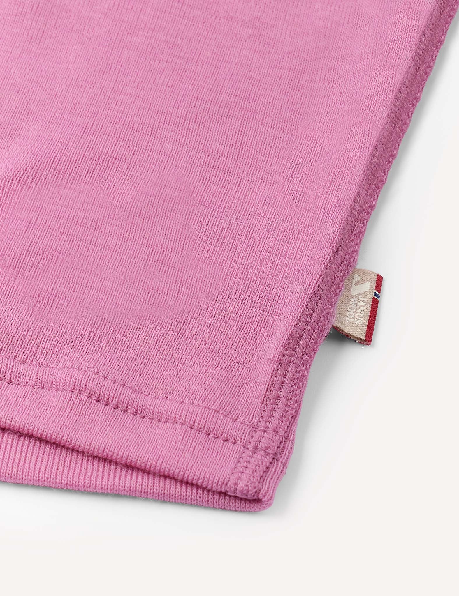Close-up of the hem of the pink Crewneck – Merino Kids Classic Rib, revealing fine ribbed wool jersey fabric, detailed stitching, and a small beige tag with text and a logo.