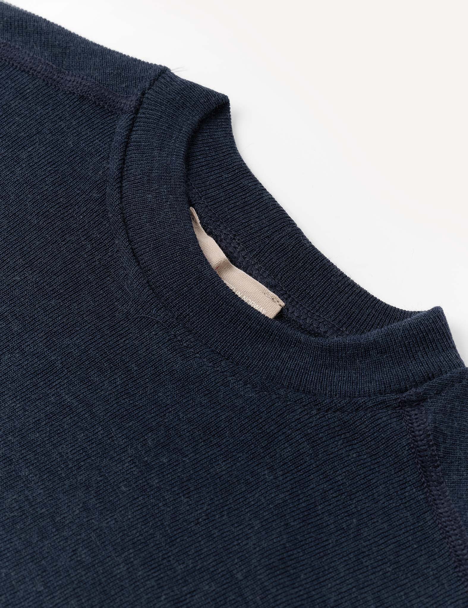 Close-up of the collar and upper chest area of the Crewneck – Merino Kids Classic Rib, a navy blue sweater made from ribbed wool jersey, shown laying flat on a light background.