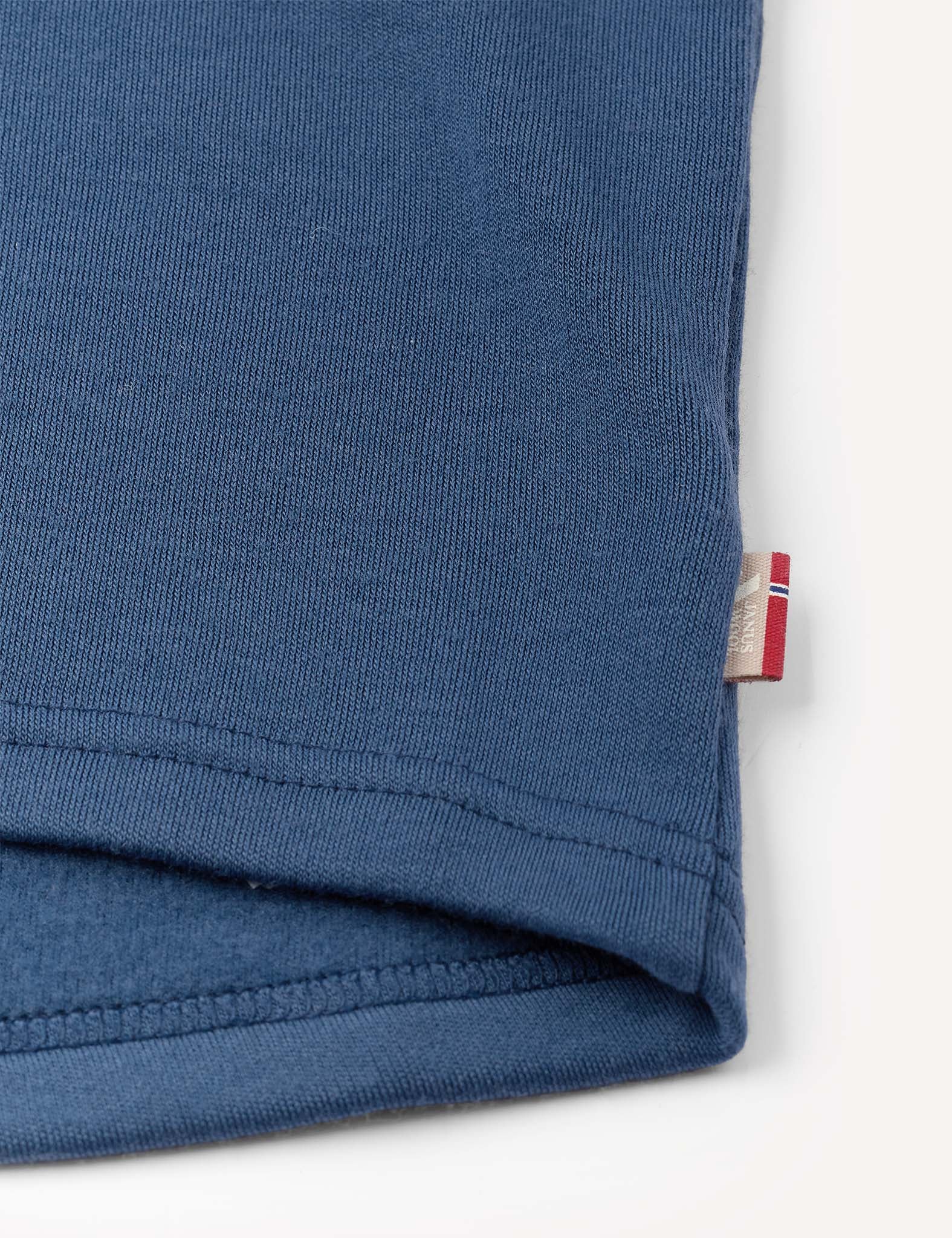Close-up of the hem of the Crewneck – Merino Kids AirWool in blue, featuring a small white and red tag sewn into the right side seam.