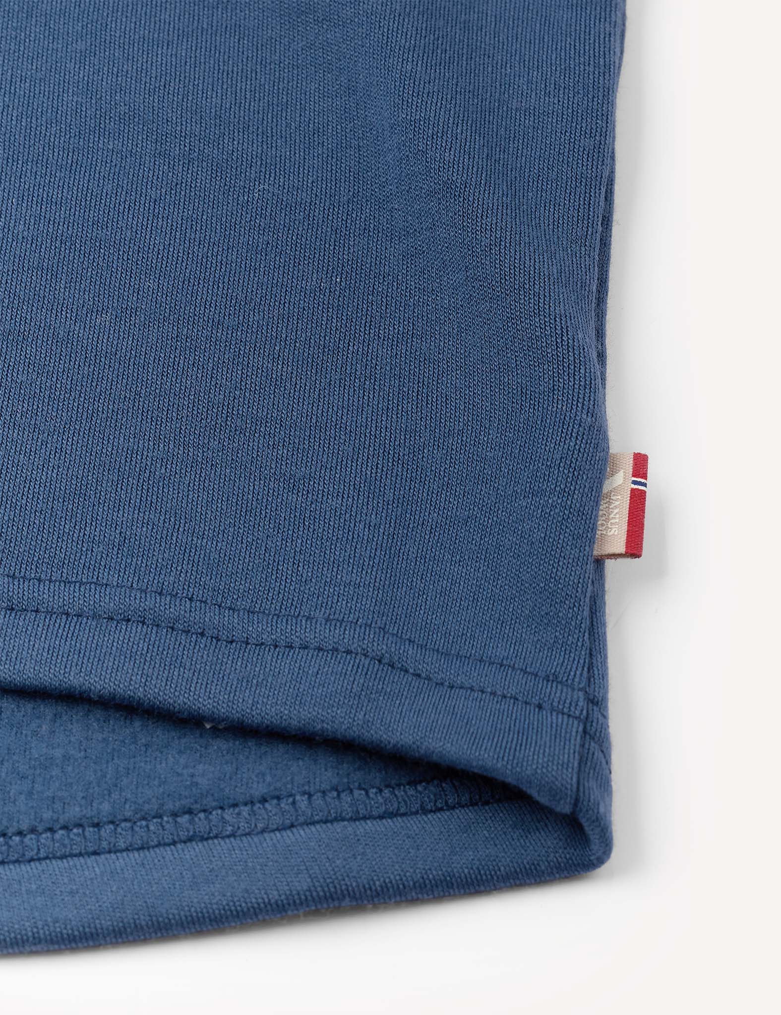 Close-up of the hem of the Crewneck – Merino Kids AirWool in blue, featuring a small white and red tag sewn into the right side seam.
