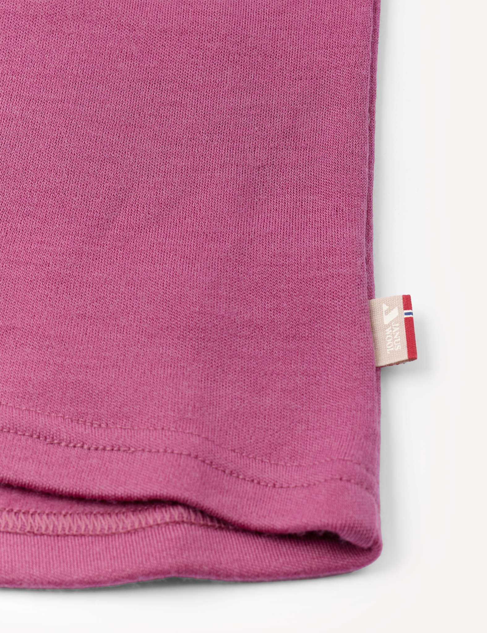 Close-up of the corner of the Crewneck – Merino Kids AirWool in pink, showing visible stitching and a small beige tag with a red and blue stripe along the right edge.