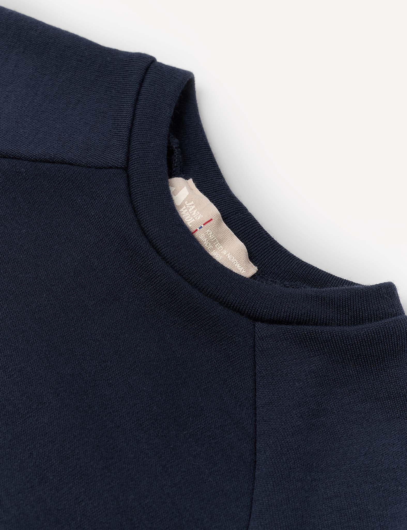Close-up of a navy blue Crewneck – Merino Kids AirWool sweatshirt, highlighting the neckline, shoulder seam, and a partially visible beige clothing tag inside the collar.