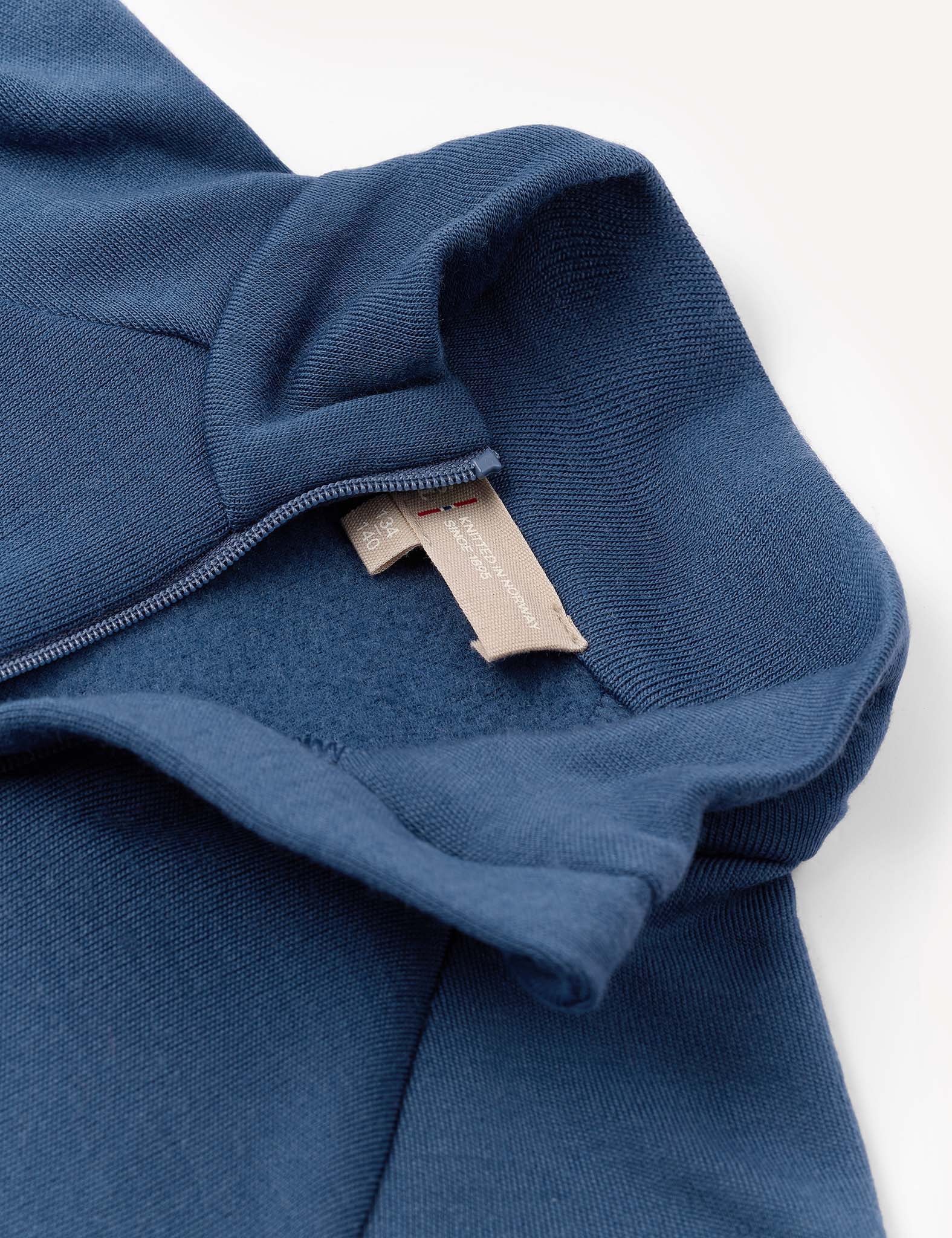 Close-up of the Half Zip – Merino Kids AirWool in blue, featuring a visible beige tag and partial zipper, with emphasis on the texture of the brushed AirWool fabric and detailed hood seam.