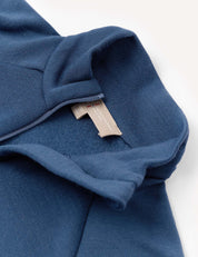 Close-up of the Half Zip – Merino Kids AirWool in blue, featuring a visible beige tag and partial zipper, with emphasis on the texture of the brushed AirWool fabric and detailed hood seam.