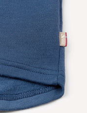 Close-up of the blue knit fabric of the Half Zip – Merino Kids AirWool, featuring a small beige tag with red, white, and blue stripes and text sewn into the edge seam.
