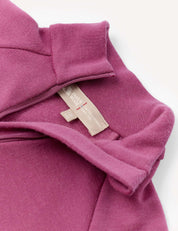 Close-up of a mauve Half Zip – Merino Kids AirWool garment featuring a brushed finish and half-zip collar, with two beige fabric labels visible: one marked 100% WOOL and the other displaying care and sizing information.