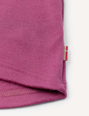 Close-up of the hem of the Half Zip – Merino Kids AirWool in pink, featuring a small fabric tag with red, white, and beige stripes sewn into the seam. The background is off-white.