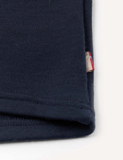 A close-up of the Half Zip – Merino Kids AirWool in navy blue, highlighting the soft merino wool fabric with visible stitching and a small tag featuring red, white, and blue stripes on the edge.