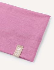 A close-up of the Headband – Merino Kids Light shows a folded pink merino wool headband with a beige tag sewn on, featuring a small white logo and text. The background is plain and light-colored.