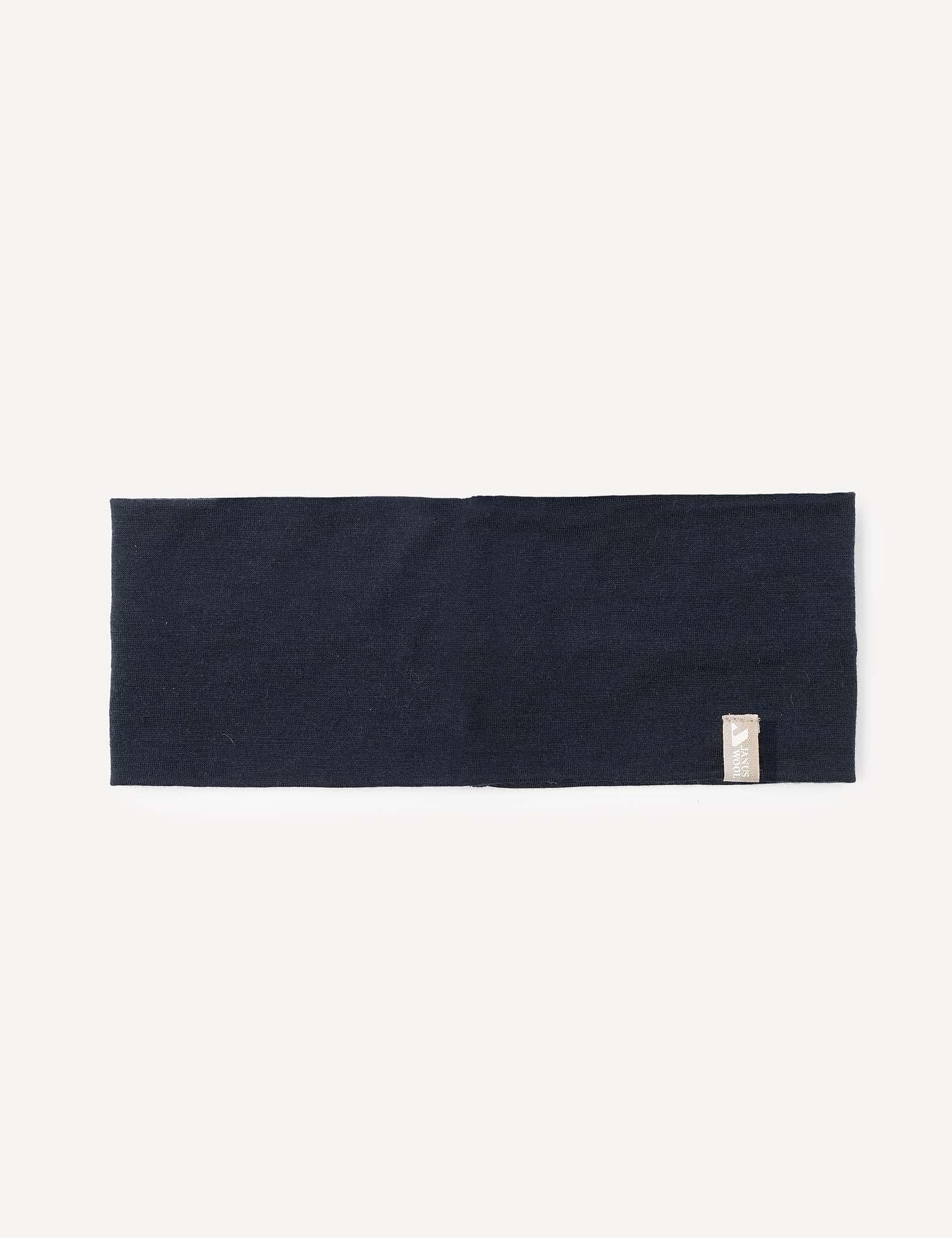 A flat, rectangular navy merino wool headband, featuring a small beige tag on one edge, is displayed against a plain white background. The Headband – Merino Kids Light offers versatile comfort for everyday use.