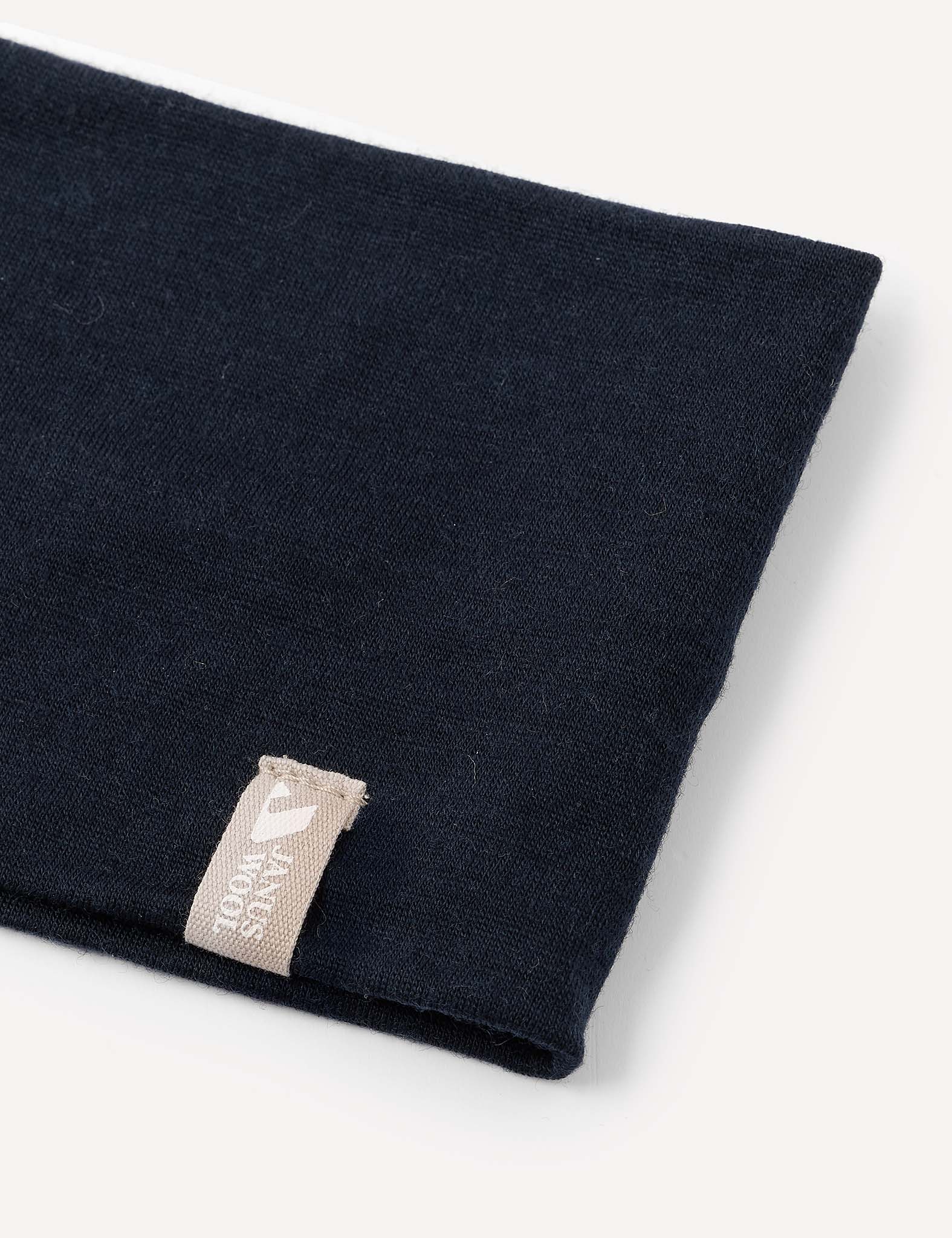 A close-up of the “Headband – Merino Kids Light,” folded in dark navy merino wool, featuring a beige tag with white text and a small heart symbol. The soft fabric is displayed against a light background.