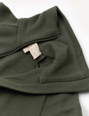 Close-up of the olive green Jacket – Merino Kids AirWool, featuring a flexible wool design with a partially unzipped collar, soft inner lining, and two beige fabric tags sewn into the neckline. The photo highlights the garment’s brushed AirWool texture and detailed construction.