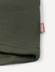 Close-up of the hem of the green Jacket – Merino Kids AirWool, showing a small fabric tag with red, white, and blue stripes sewn into the side seam.