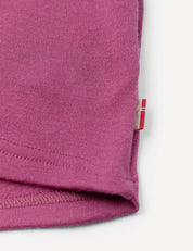 Close-up of a hemmed edge of a pink fabric, likely a t-shirt sleeve, featuring a small tag with a red and white stripe pattern sewn into the seam, highlighting details reminiscent of the Jacket – Merino Kids AirWool craftsmanship.