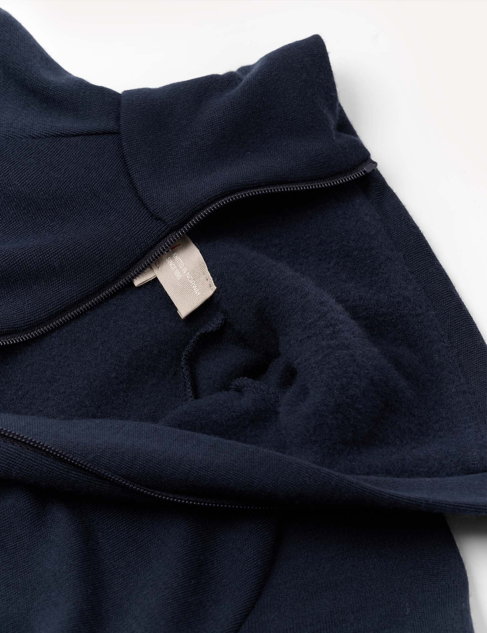 A close-up of the Jacket – Merino Kids AirWool in navy blue, partially unzipped to reveal a beige fabric tag inside. The material looks soft and fleece-lined, highlighting the cozy comfort typical of brushed AirWool merino wool.