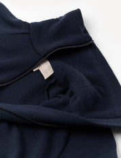 A close-up of the Jacket – Merino Kids AirWool in navy blue, partially unzipped to reveal a beige fabric tag inside. The material looks soft and fleece-lined, highlighting the cozy comfort typical of brushed AirWool merino wool.