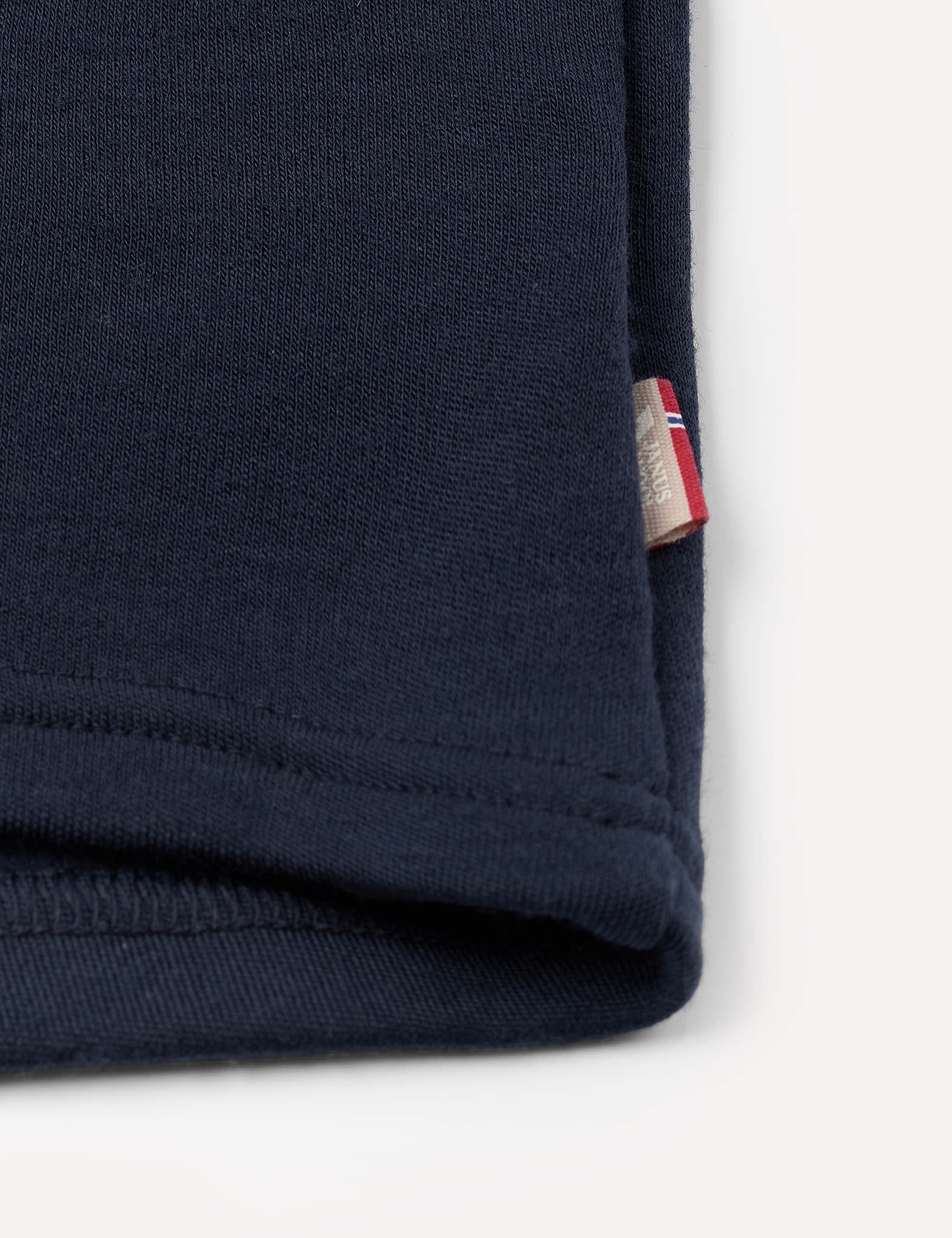 A close-up of the Merino Kids AirWool jacket in dark navy blue features soft brushed AirWool fabric with neatly stitched edges and a small beige tag displaying a partial red, white, and blue design, possibly part of a logo or flag. The background is plain white.