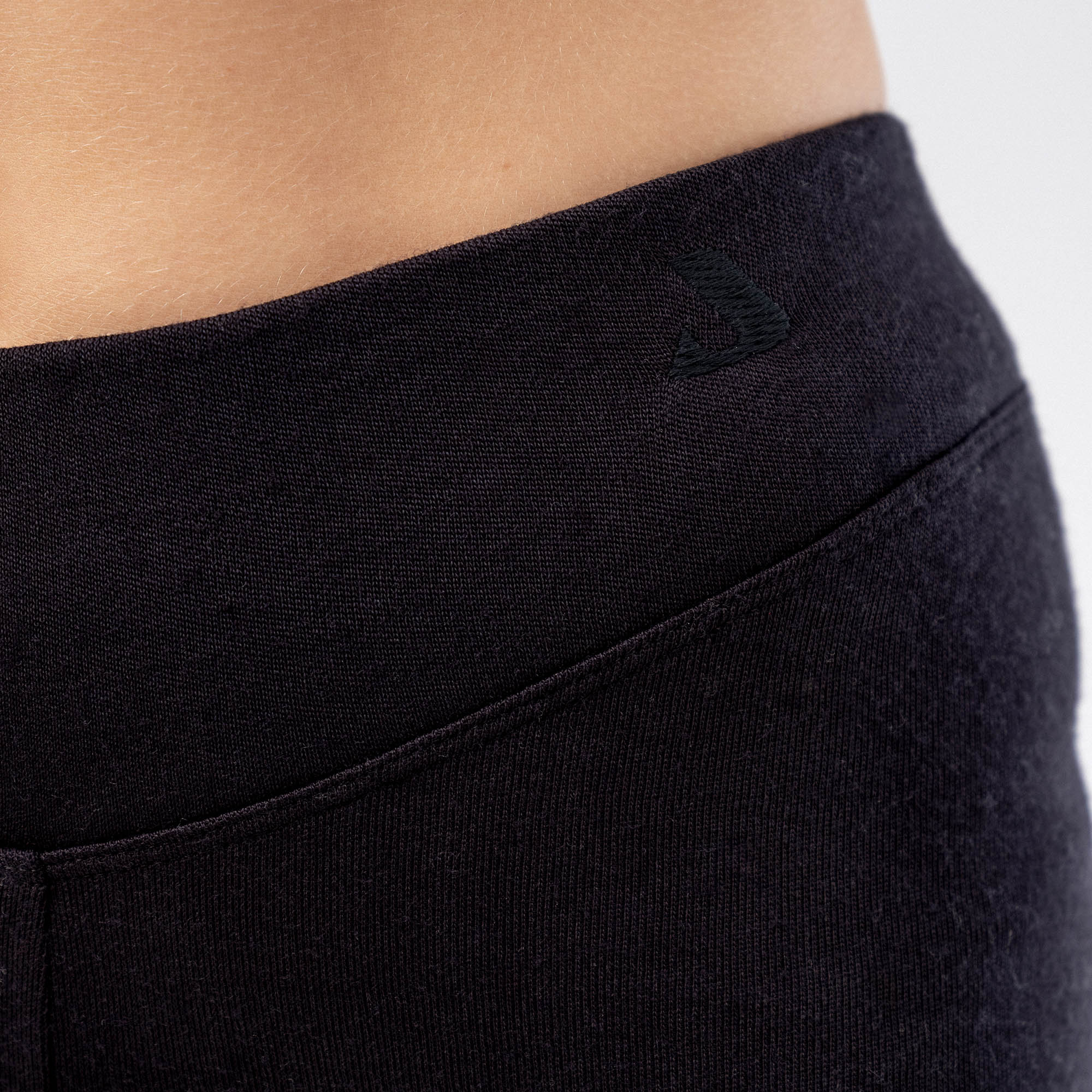 Close-up of a person wearing Leggings Merino – AirWool 260 Women, showcasing the waistband and subtle left hip logo against a light background, emphasizing warmth and breathability.