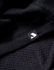 Close-up of the Norse Merino Unisex Double Layer Jacket in black showcasing its textured yet smooth fabric, with a small black tag featuring a white geometric logo.