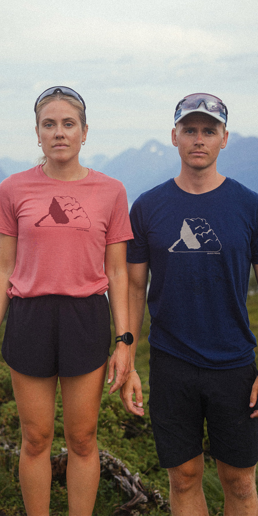 Two people with Janus merino t-shirts standing in front of a scenic mountain landscape with a lake.