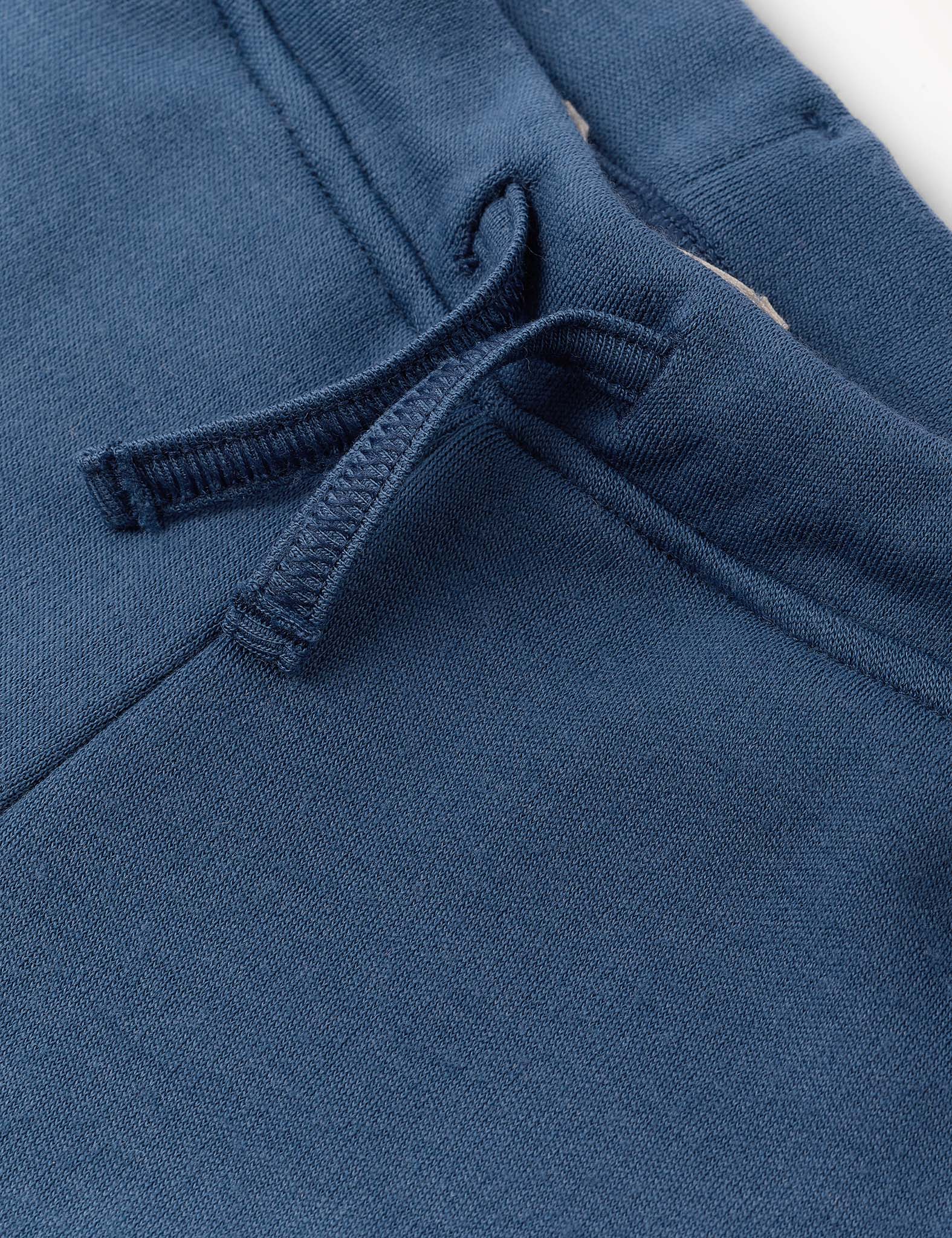 Close-up of blue Merino Kids AirWool sweatpants fabric showing a drawstring and part of a pocket, highlighting the texture and stitching details.