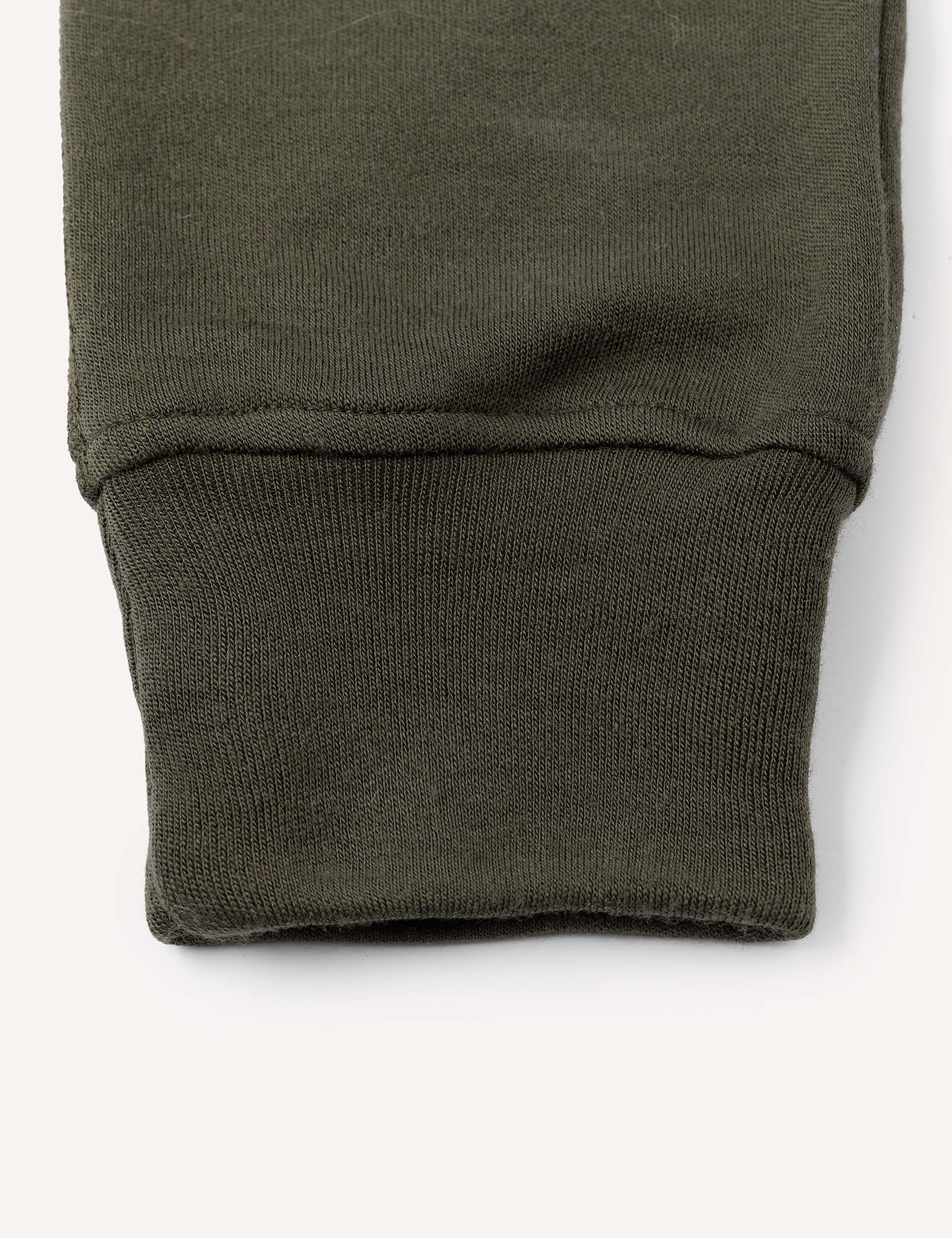 Close-up of an olive green fabric cuff, likely the sleeve or pant leg cuff of a garment such as the Sweatpants – Merino Kids AirWool, shown against a plain light background.