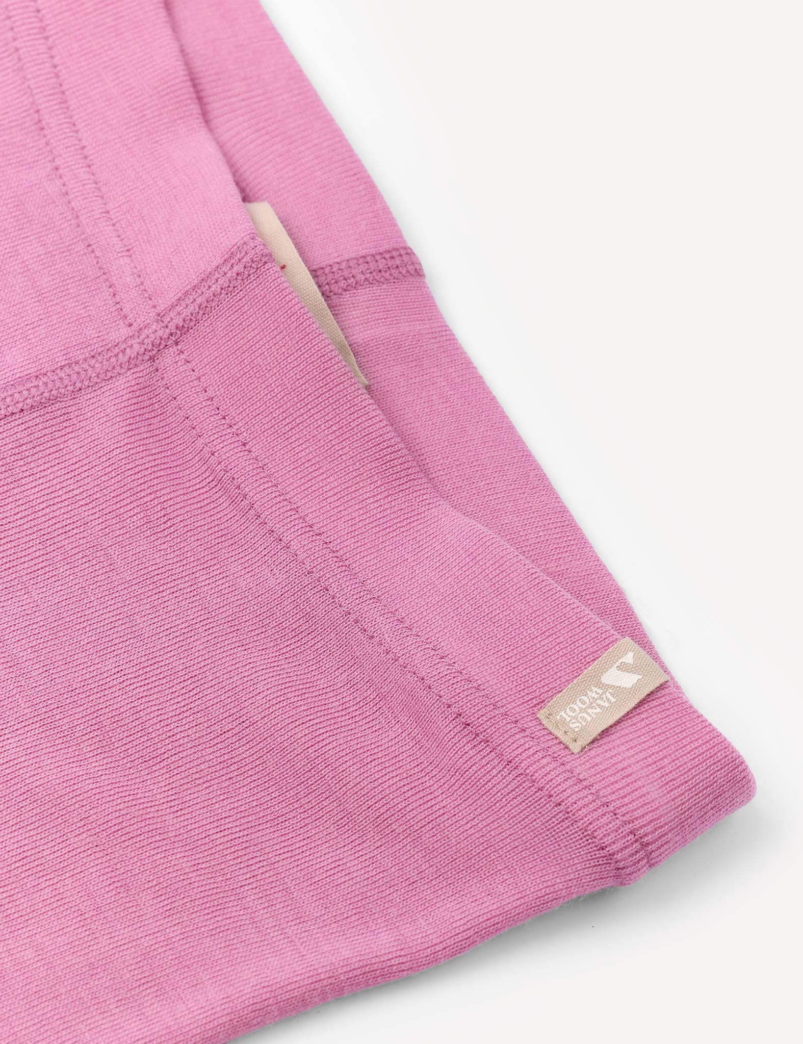 Close-up of the Leggings – Merino Kids Classic Rib in pink, featuring visible stitching and elastic detailing, a cream-colored tag partially tucked into the seam, and a small fabric label reading “Roomy Comfy” sewn near the edge.