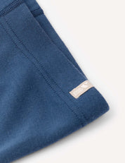 Close-up of a blue fabric garment—the Leggings – Merino Kids AirWool—crafted from brushed AirWool, featuring a stitched seam and a small beige tag with white text and logo, set against a plain light background.